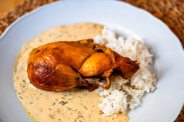 Roasted chicken leg with dill sauce and rice on plate.