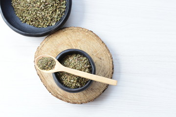Chopped dried leaves of basil leaves on white wooden background