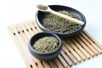 Chopped dried leaves of basil leaves on white wooden background