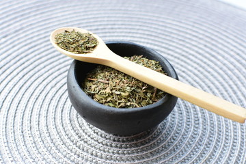 Chopped dried leaves of basil leaves on white wooden background