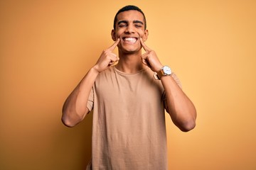 Young handsome african american man wearing casual t-shirt standing over yellow background Smiling...