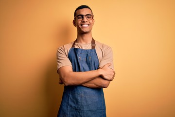 Young handsome african american shopkeeper man wearing apron over yellow background happy face...