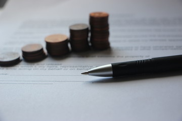 Pen and coins stacks reminding growth diagramm on agreement background. Successfully Growing Business concept