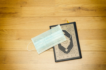 Holy Quran with Arabic calligraphy meaning of Al Quran  and medical mask on wood table