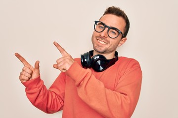 Young handsome man listening to music using headphones over isolated white background smiling and looking at the camera pointing with two hands and fingers to the side.