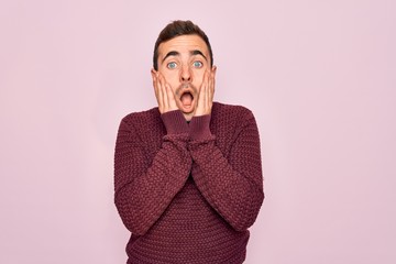 Young handsome man with blue eyes wearing casual sweater standing over pink background afraid and shocked, surprise and amazed expression with hands on face
