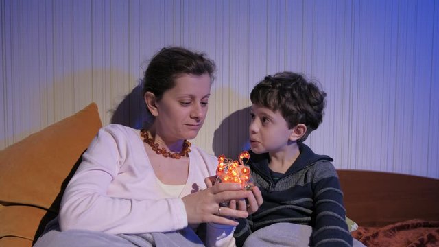 Mother and son sitting on bed with lamps in hands and telling bedtime stories