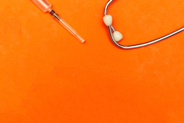 portrait of stethoscope and syringe on orange background with copy space