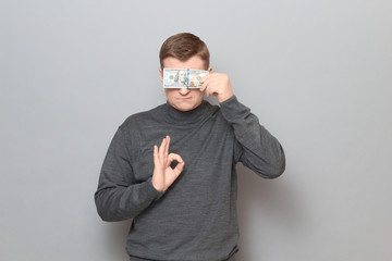 Man is covering his eyes with money and showing okay gesture