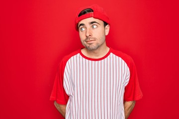 Young handsome sporty man with blue eyes wearing striped baseball t-shirt and cap smiling looking to the side and staring away thinking.