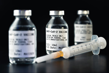 Coronavirus Covid-19 vaccine concept -  three glass vials on black table, hypodermic syringe near closeup detail (label own design - dummy data, not real product)