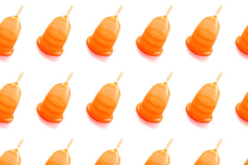 Pattern made from orange menstrual cup on white background.