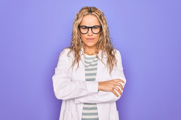 Young beautiful blonde scientist woman wearing coat and glasses over purple background skeptic and nervous, disapproving expression on face with crossed arms. Negative person.