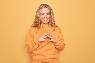 Young beautiful blonde sporty woman wearing casual sweatshirt over yellow background Hands together and fingers crossed smiling relaxed and cheerful. Success and optimistic