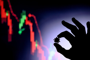 Graphs representing the stock market crash caused by the Coronavirus. Hands silhouette holds covid 19 virus