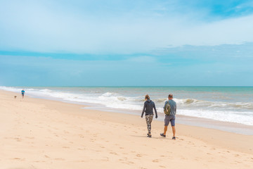 Back view of people walking on a beautiful deserted beach natural seascape cloudy sky landscape outdoors background.