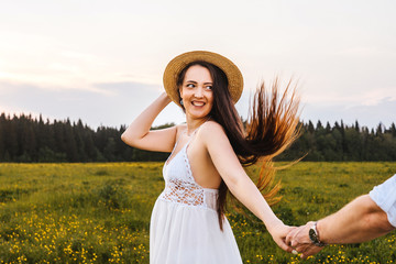 Young pregnant woman in the field hold husbands hand. Sunset light.