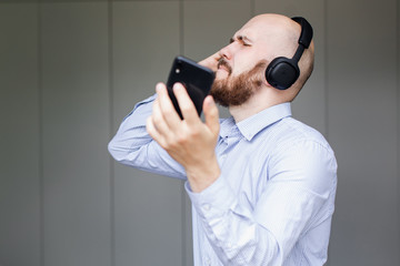 Naklejka premium a bearded bald man sings songs and listens to music with headphones at home