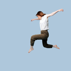 Fototapeta premium Young woman doing figure jump over blue background.