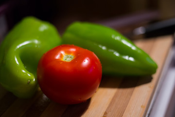 Close up view on one fresh tomato and two paprikas on wooden kitchen board.