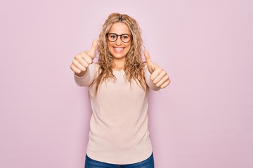 Young beautiful blonde woman wearing casual sweater and glasses over pink background approving doing positive gesture with hand, thumbs up smiling and happy for success. Winner gesture.