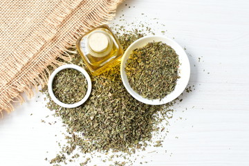 Dried chopped leaves of basil leaves and olive oil on white wooden background