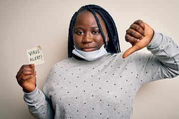 African american woman wearing medical mask holding reminder with virus alert message with angry...