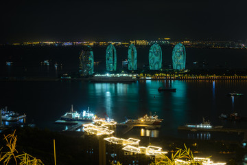 Fototapeta na wymiar Night view of the Phoenix island in the Sanya city with bright multi-colored illumination buildings, structures and ships. Sanya Phoenix Island President Resort Apartment.