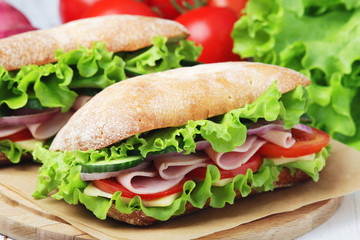 Two sandwiches with fresh vegetables, ham and cheese in ciabatta bread