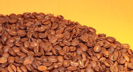 Coffee beans on a bright background. Coffee granules on an orange table. Texture of coffee beans.