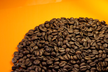 Coffee beans on a bright background. Coffee granules on an orange table. Texture of coffee beans.
