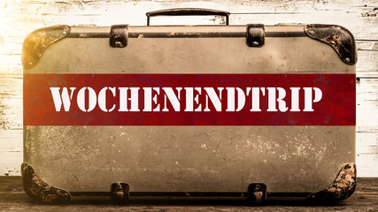 URLAUB HINTERGRUND - Alter rustikaler vintage Koffer mit rotem Banner und weißem Schriftzug "WOCHENENDTRIP"