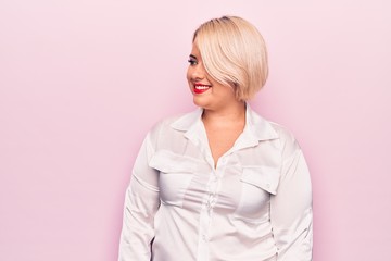 Young beautiful blonde plus size woman wearing elegant shirt over isolated pink background looking to side, relax profile pose with natural face and confident smile.