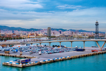 Fototapeta na wymiar Barcelona, Spain. Porta d’Europa bascule bridge over Barcelona Port and Wharfs, with Torre Jaume I aerial lift steel truss tower, mountains, city skyline architecture in background.