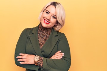 Young beautiful blonde plus size woman wearing elegant jacket over isolated yellow background happy face smiling with crossed arms looking at the camera. Positive person.