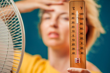 A portrait of woman in front of fan suffering from heat holding thermometer. Close up. Hot weather...