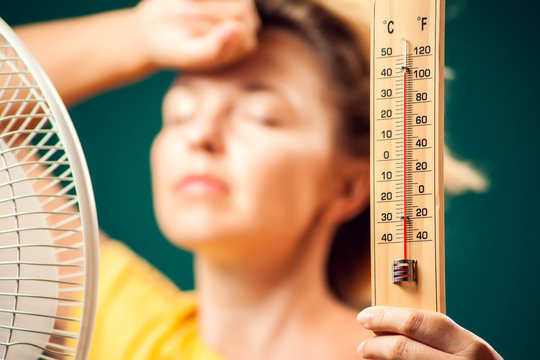 A portrait of woman in front of fan suffering from heat holding thermometer. Close up. Hot weather concept