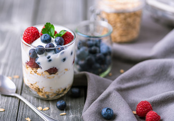 White yogurt in glass jar with raspberries and blueberries on grey napkin.