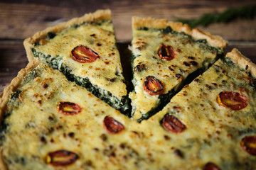 Homemade cheesy spinach quiche for brunch. set on wooden cafe table background.