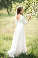 Fototapeta na wymiar Beautiful young girl with long hair in a white dress with an open back in a summer blooming garden