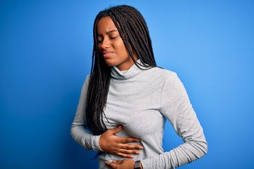 Young african american woman standing wearing casual turtleneck over blue isolated background with hand on stomach because indigestion, painful illness feeling unwell. Ache concept.