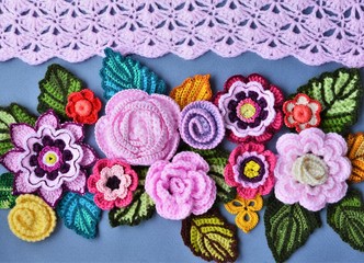 Decorative flat lay from crocheted flowers and leaves on a grey and pink background.
