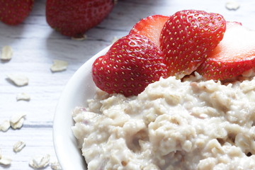 Oatmeal porridge with fresh strawberries on a wooden background.