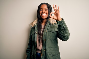Young african american woman wearing winter parka coat over isolated background smiling positive doing ok sign with hand and fingers. Successful expression. - obrazy, fototapety, plakaty