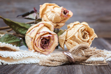 Wedding rings and roses dried flowers on wooden background