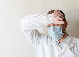 A sad, tired male doctor in a medical mask put his hand on his head. Overload due to a large number...
