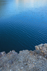 Obraz premium Stone rocks near water, on the background of lake, river, sea, ocean. Blue clear water. Artificial reservoirs