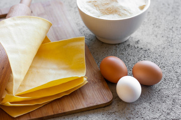 Ingredients for homemade lasagna. Rolling pin, flour, eggs and fresh lasagna sheets. Selective focus
