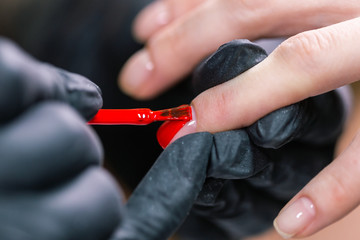 Close Up shot of master in rubber gloves covering red nails with top coat in the beauty salon. Perfect nails manicure process. - obrazy, fototapety, plakaty