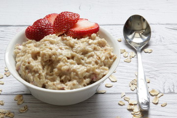 Oatmeal porridge with fresh strawberries on a wooden background.